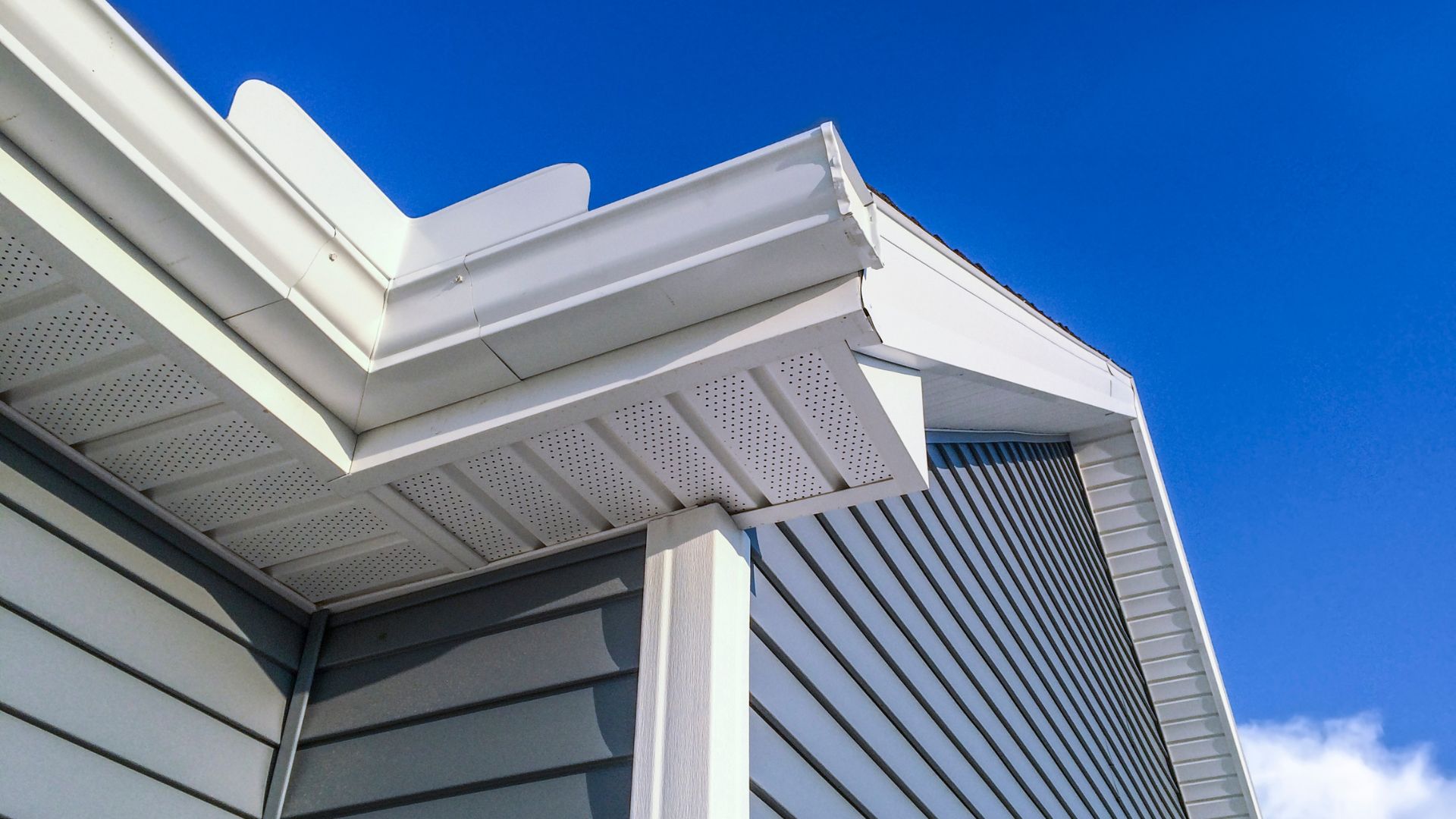 Modern white building corner with perforated soffit and blue sky
