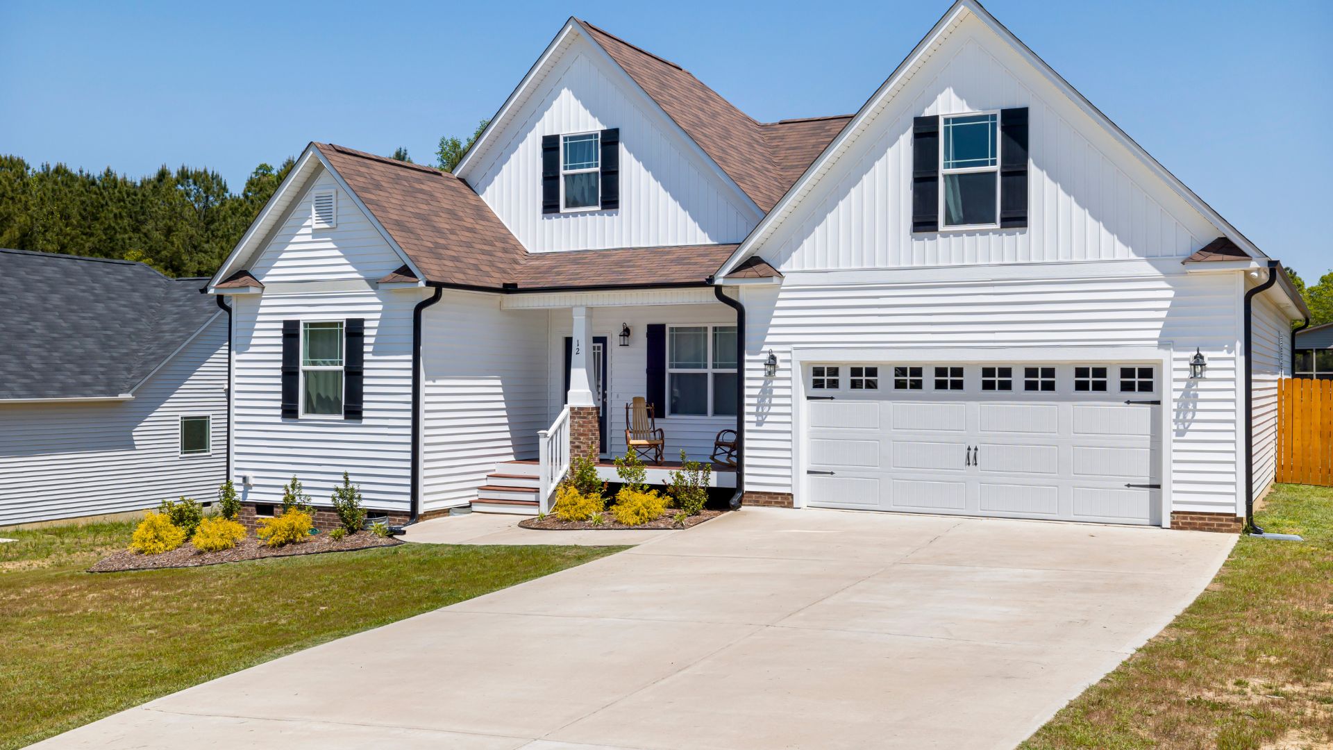 White two-story house with black shutters, attached garage, and yellow landscaping